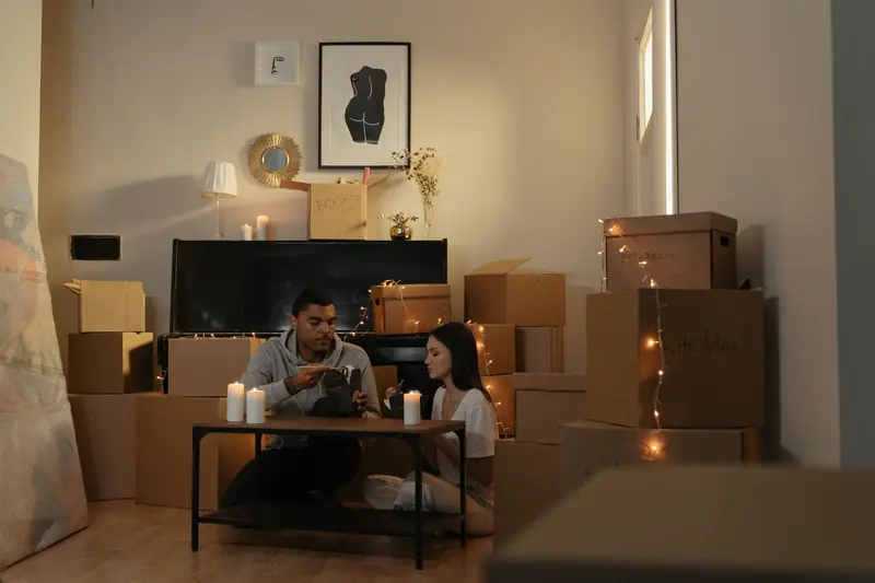 A couple sits surrounded by boxes and candles, creating a cozy atmosphere while settling into their new apartment