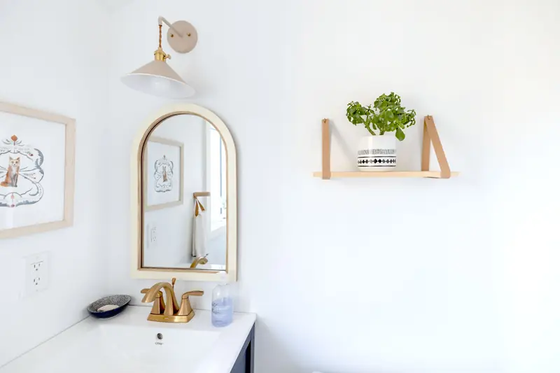 Bright and simple bathroom interior with a gold-framed mirror and decorative shelf