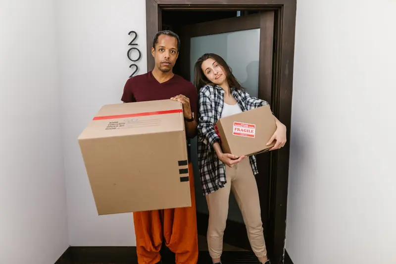 A couple carrying moving boxes indoors, settling into their new apartment